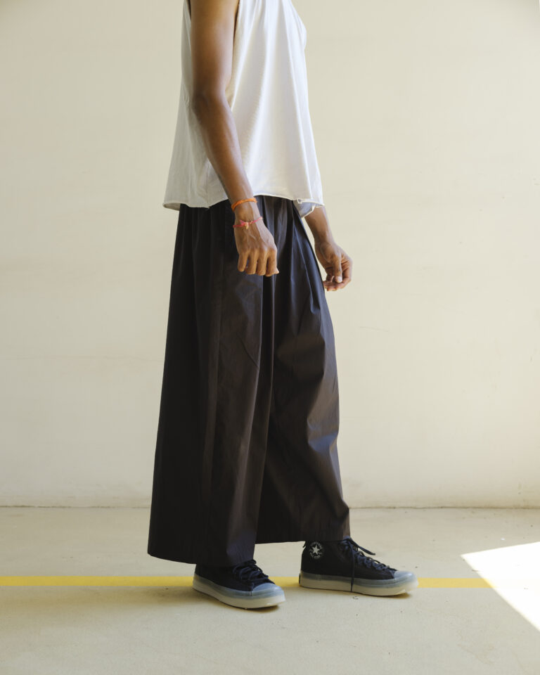 Side profile of Now + Thenn men’s wide-leg black cotton trousers styled with casual streetwear sneakers and sleeveless white tee.