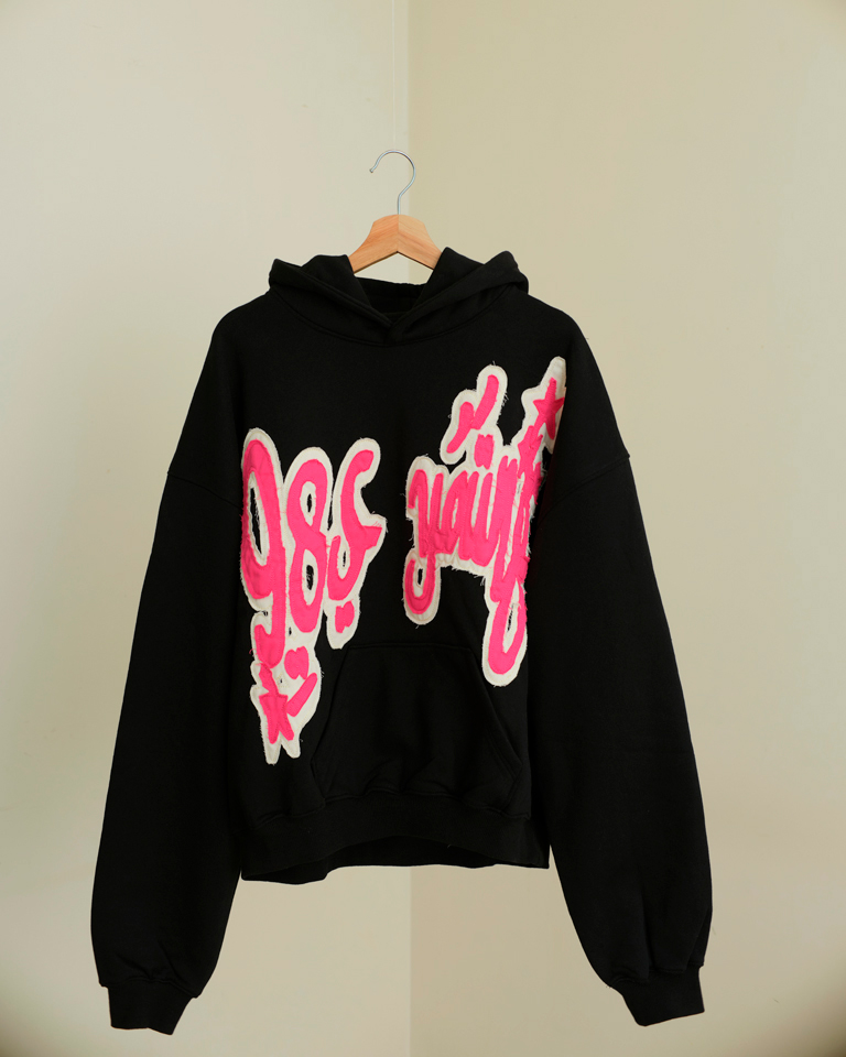 Black oversized hoodie with bold pink chenille graffiti patch and relaxed fit from Now + Thenn.