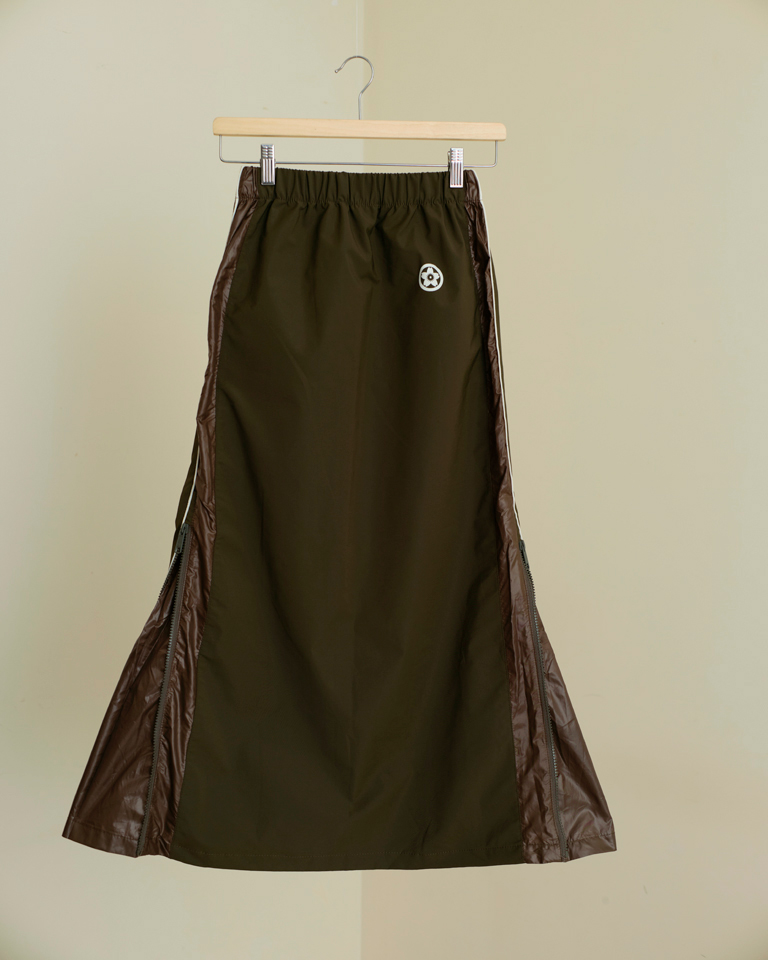 Olive utility midi skirt with side zip panels, reflective piping, elastic waist, and relaxed fit, styled with layered streetwear looks.