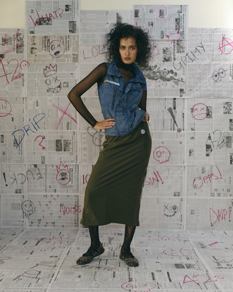 Olive utility midi skirt with side zip panels, reflective piping, elastic waist, and relaxed fit, styled with layered streetwear looks.