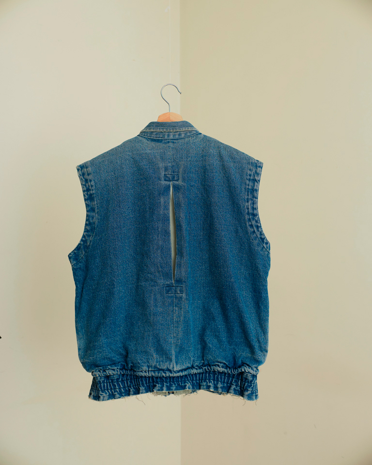 Upcycled vintage denim utility vest by Now + Thenn featuring contrast patchwork panels, zip pockets, snap buttons and elastic hem in a unisex sleeveless jacket design.