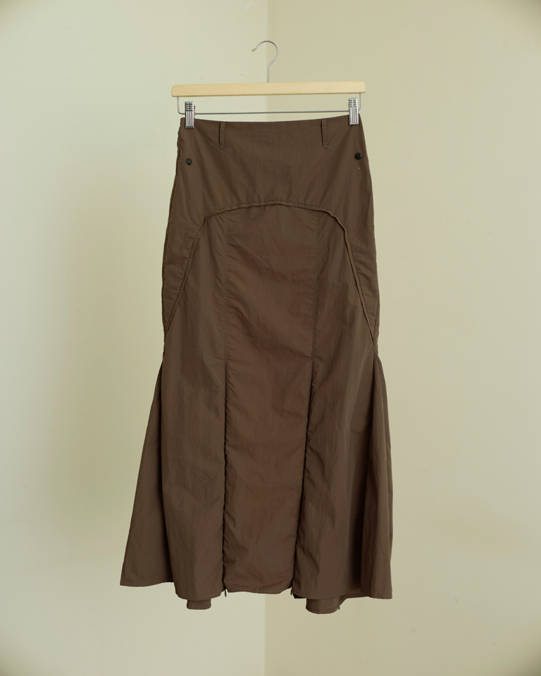 Brown panelled midi skirt with detachable utility pockets and zipper slit detail, structured modern silhouette by Now + Thenn.