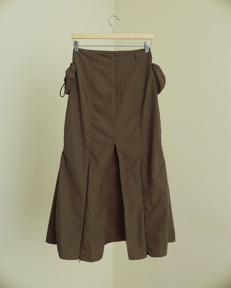 Brown panelled midi skirt with detachable utility pockets and zipper slit detail, structured modern silhouette by Now + Thenn.