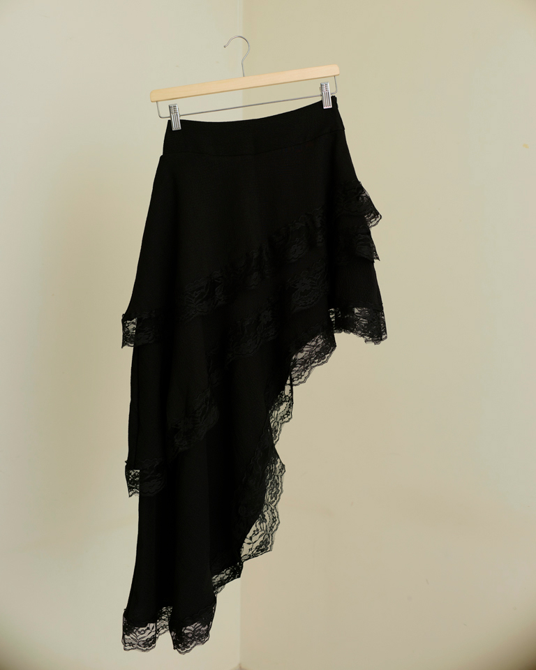 Black asymmetric high-low skirt with layered lace trim panels and fluid draped silhouette by Now + Thenn