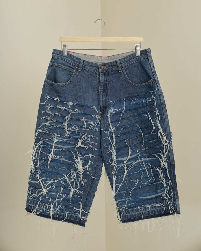 Upcycled shredded denim jorts featuring distressed horizontal panel detailing, exposed frayed threads and a relaxed oversized fit crafted from reclaimed denim.