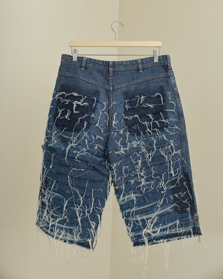 Upcycled shredded denim jorts featuring distressed horizontal panel detailing, exposed frayed threads and a relaxed oversized fit crafted from reclaimed denim.