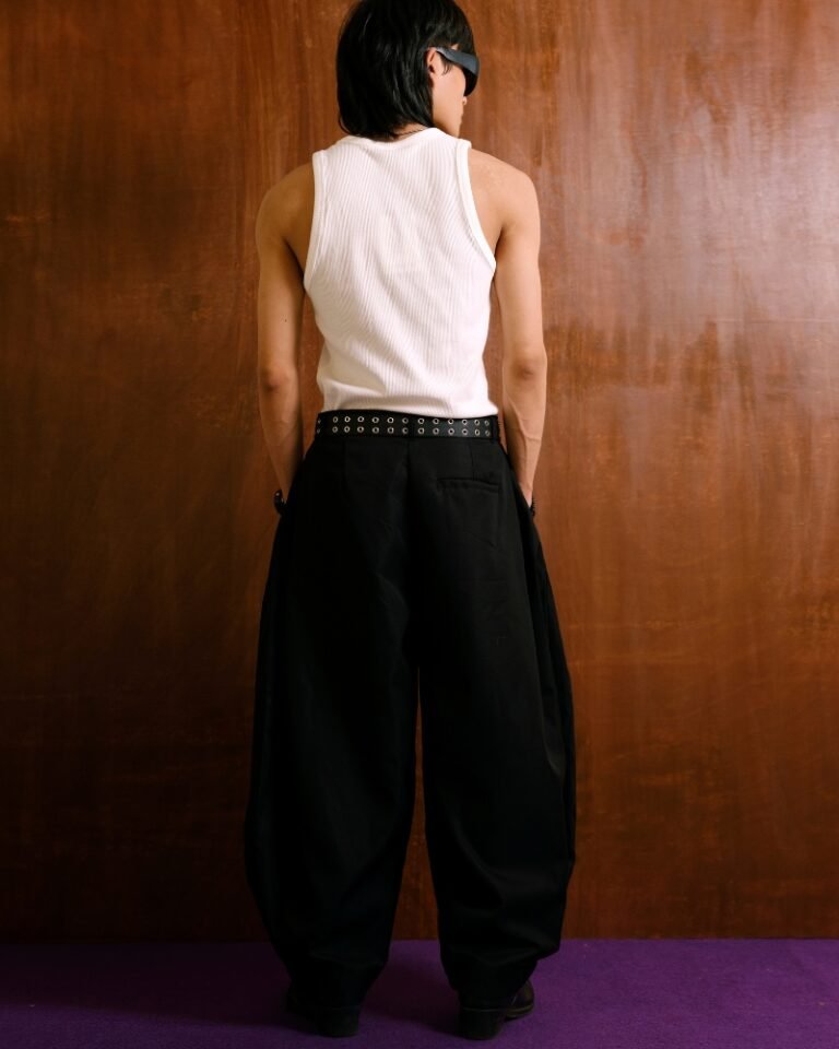 Black pleated trousers with a dramatic balloon-leg silhouette and tapered ankle cuffs, shown on a hanger and worn front, side and back.