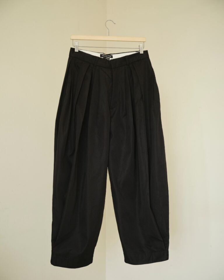 Black pleated trousers with a dramatic balloon-leg silhouette and tapered ankle cuffs, shown on a hanger and worn front, side and back.