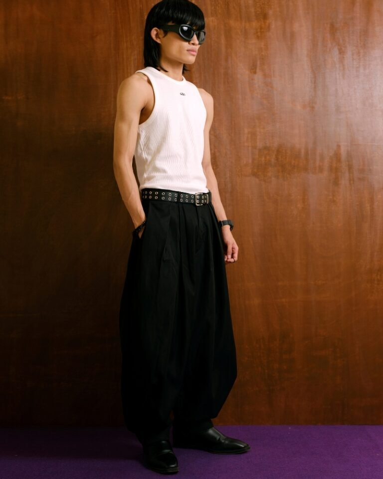 Black pleated trousers with a dramatic balloon-leg silhouette and tapered ankle cuffs, shown on a hanger and worn front, side and back.
