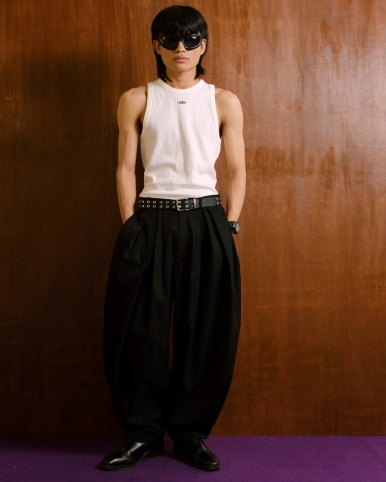 Black pleated trousers with a dramatic balloon-leg silhouette and tapered ankle cuffs, shown on a hanger and worn front, side and back.