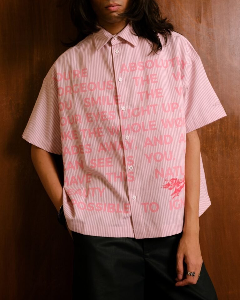 Pink and white striped shirt with an allover pink love-note text print, shown worn with black trousers.