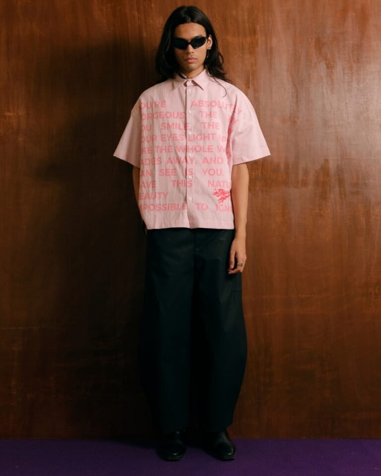 Pink and white striped shirt with an allover pink love-note text print, shown worn with black trousers.